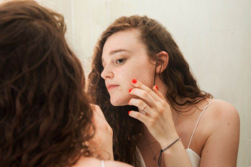 Young teenager looks in the mirror while checking her face for acupuncture treatment for teens blog.
